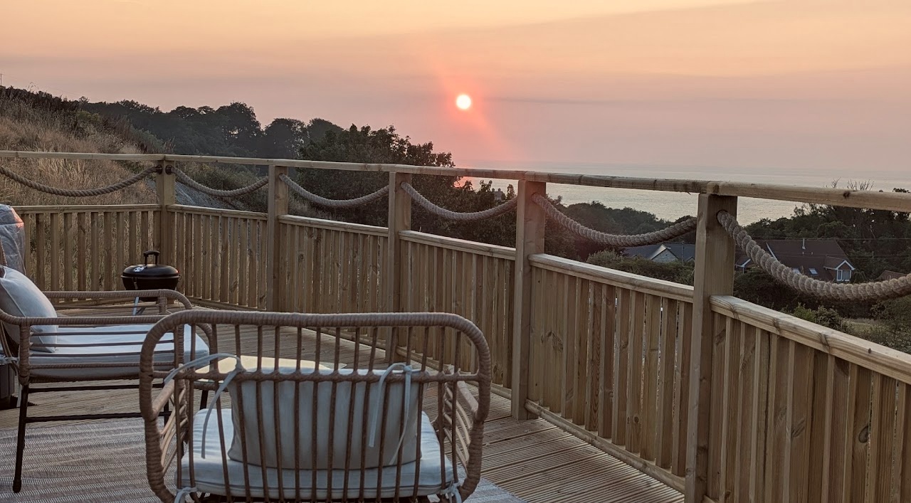 Glamping pod view from decking of sun set into the sea over Tresaith, Cardigan Bay